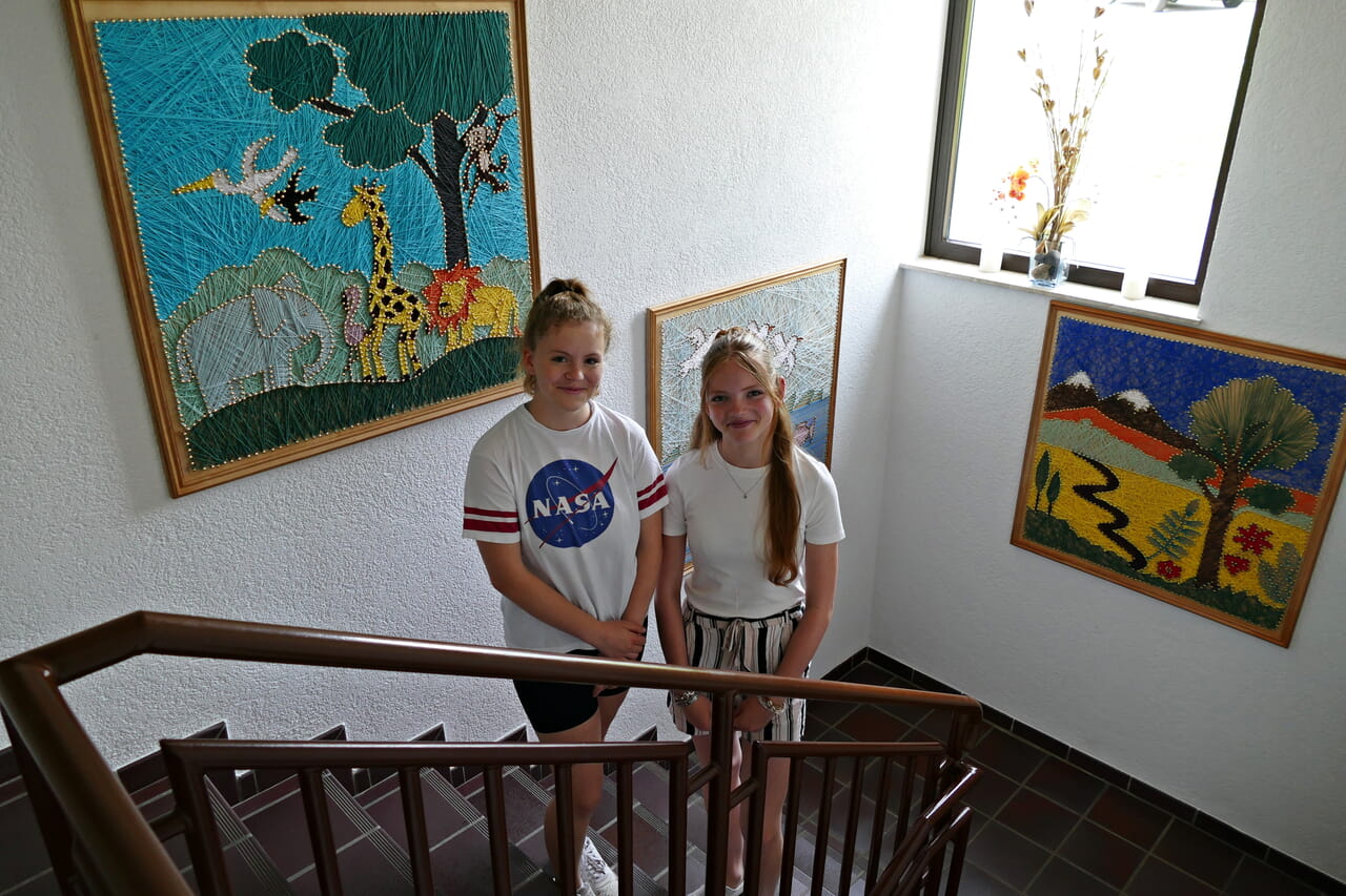 Die Mitarbeiterinnen Anna 15, l.) und Lena (14) sind zum dritten Mal mit dabei. Die Bilder, die im Treppenhaus des Evangelischen Gemeindezentrums Wenden hängen, haben sie mitgestaltet bei der Kinder-Kunst-Woche 2022.